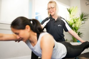 A female physiotherapist helping a woman stretch her arm and leg outwards.