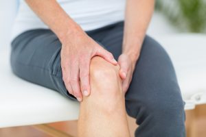 A close up image of someone with their right trouser leg pulled up above the knee, whilst they tightly grip their knee.