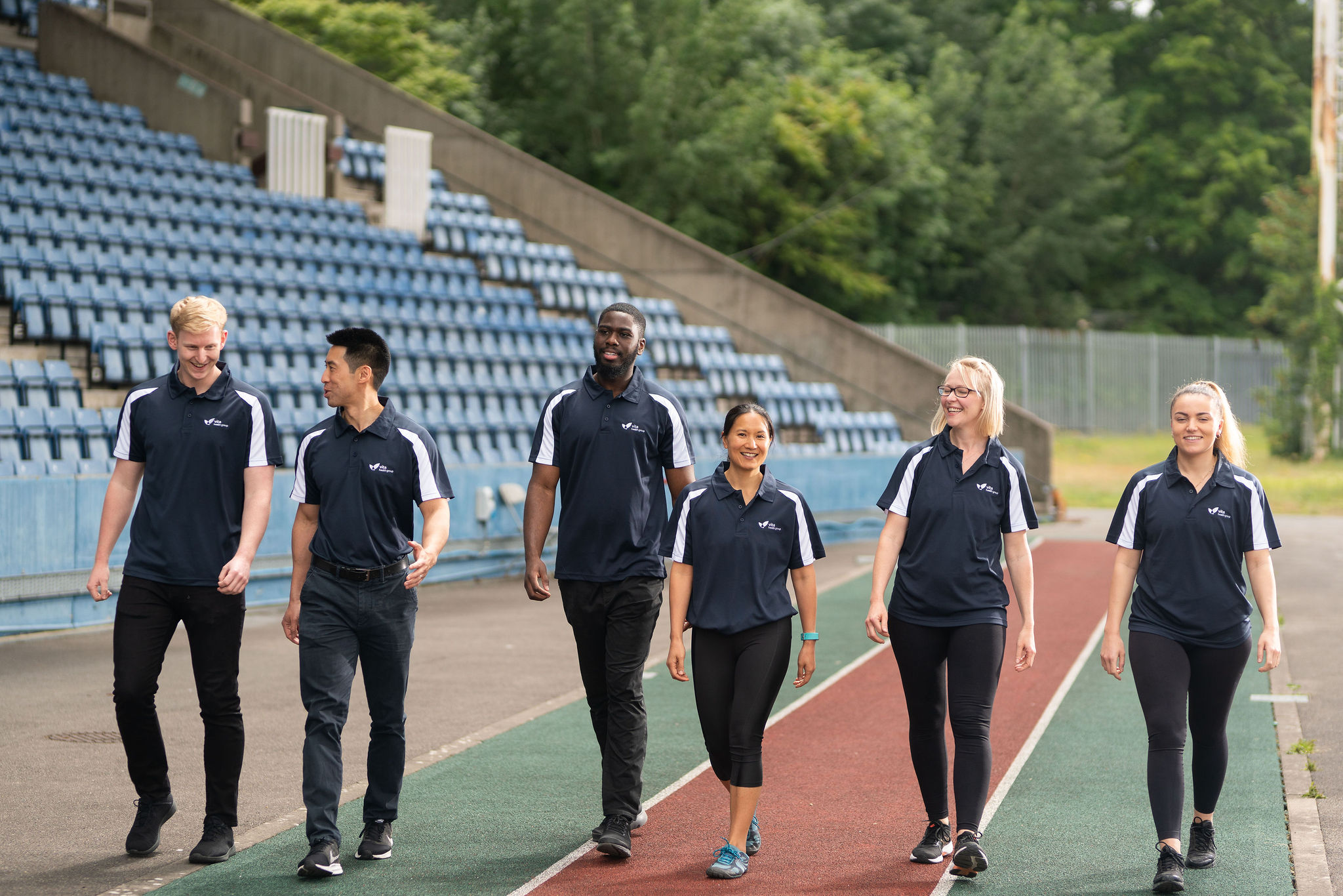 Six staff members walk together on a running track smiling and talking